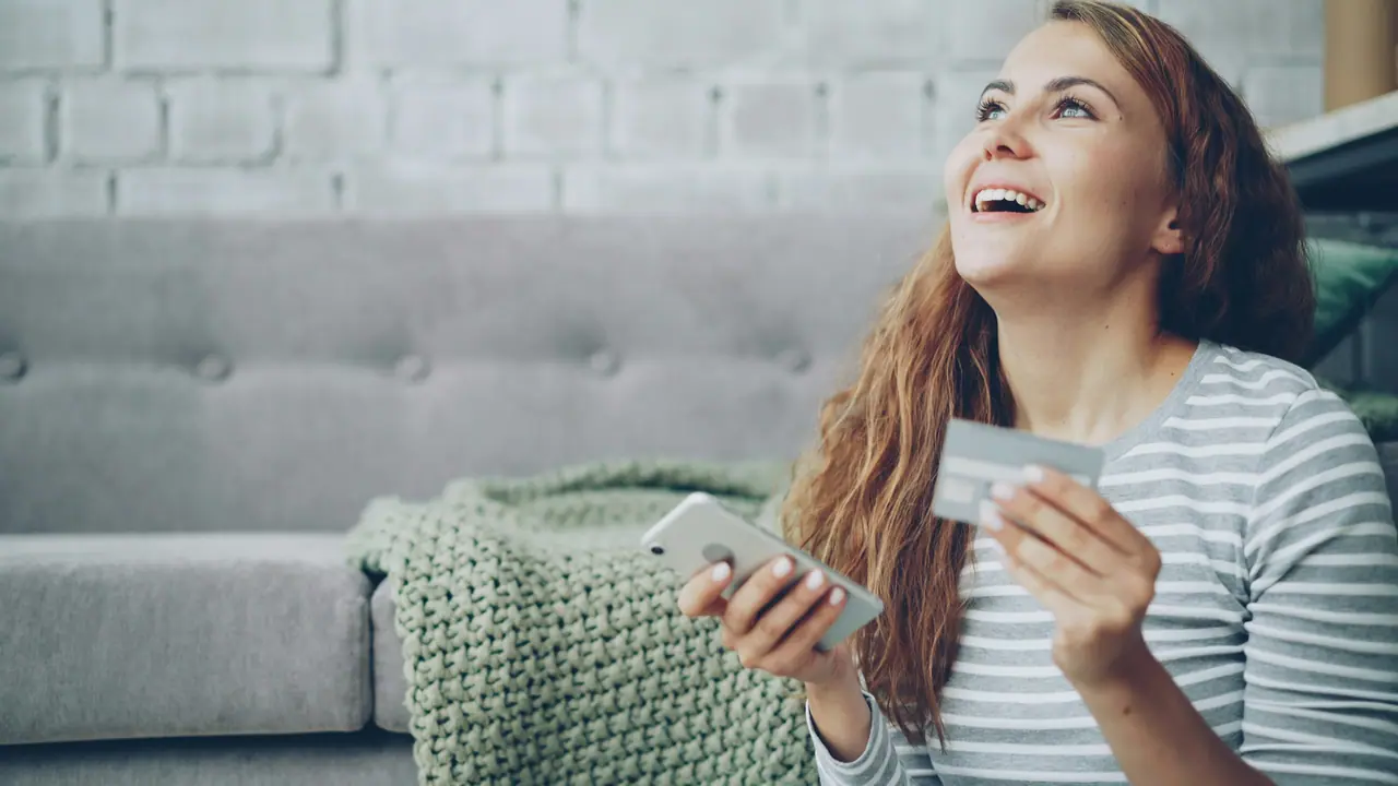 Mulher no sofá com cartão e celular na mão